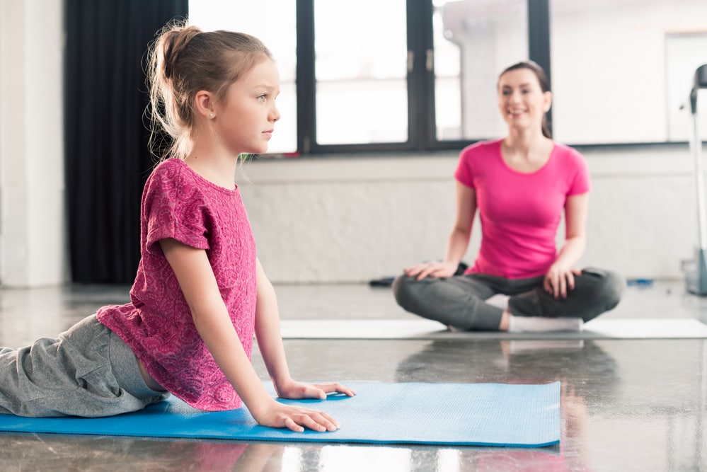girl in Cobra pose with yoga teacher in background