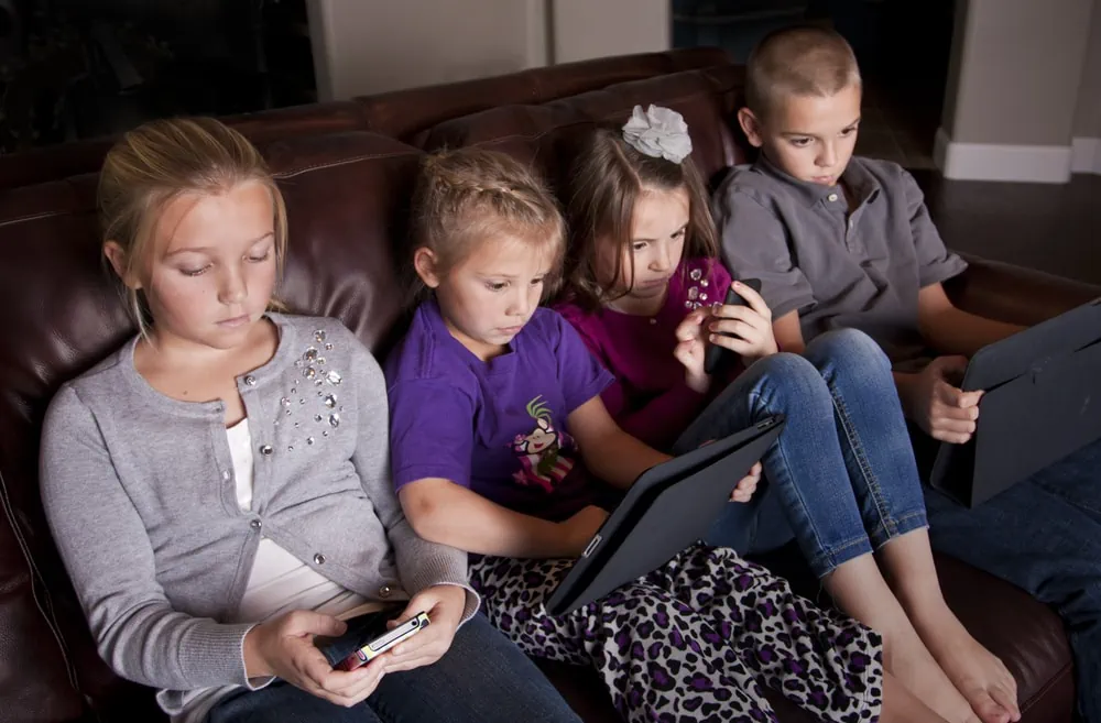 kids on couch ignoring each other using mobile devices